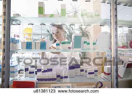 Stock Image - Pharmacist in pharmacy looking at medicine box. Fotosearch