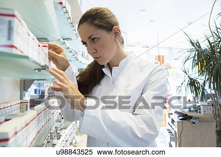 Stock Photography - Pharmacist in pharmacy looking at medicine box. Fotosearch