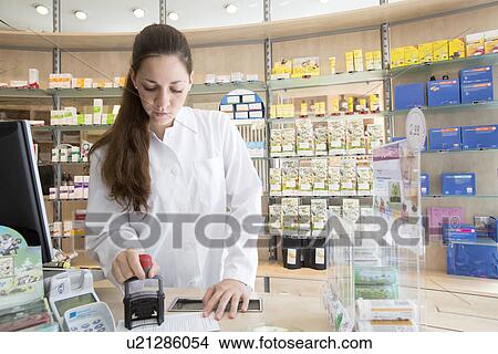 Pharmacist in pharmacy stamping prescription View Large Photo Image Picture - Pharmacist in pharmacy stamping prescription. Fotosearch