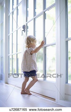 Stock Photography - Portrait female toddler looking out of patio doors. Fotosearch