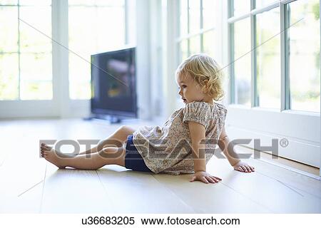 Stock Photography - Portrait female toddler sitting on living room floor. Fotosearch