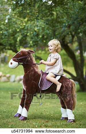 Portrait of female toddler riding toy horse in garden View Large Photo Image Picture - Portrait of female toddler riding toy horse in garden. Fotosearch