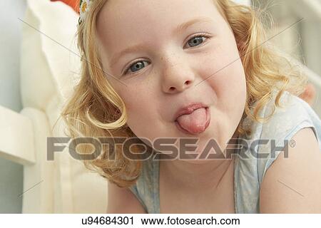 Stock Image - Portrait of girl lying on seat sticking tongue out. Fotosearch