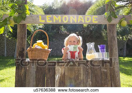 Stock Photo - Portrait of girl on lemonade stand holding up one hundred euro note. Fotosearch