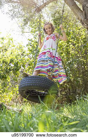 Portrait of girl standing swinging on tree swing in garden View Large Photo Image Stock Image - Portrait of girl standing swinging on tree swing in garden. Fotosearch