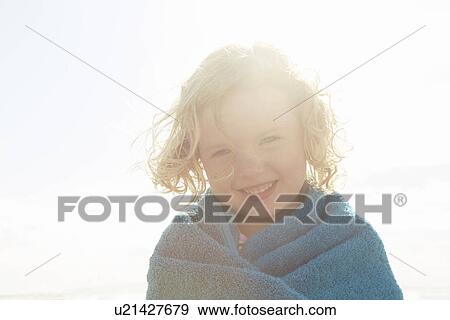 Stock Photo - Portrait of girl wrapped in towel at sunlit coast. Fotosearch