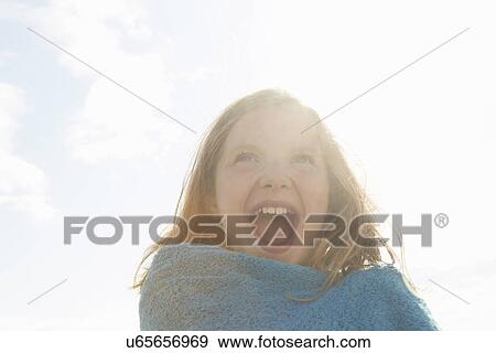Stock Photo - Portrait of laughing girl wrapped in towel at sunlit coast. Fotosearch