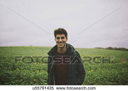 Portrait of smiling young man standing in field View Large Photo Image Stock Photography - Portrait of smiling young man standing in field. Fotosearch