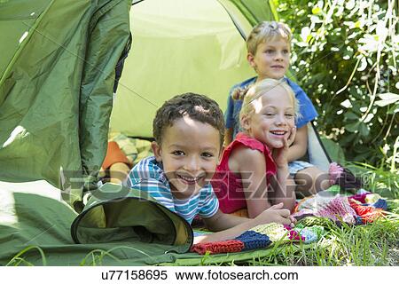 Stock Photography - Portrait of three smiling children lying in garden tent. Fotosearch