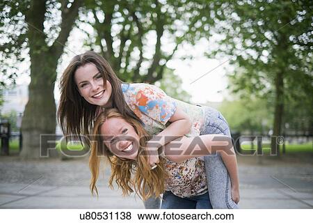 Portrait of two young female best friends giving piggy back in park View Large Photo Image Stock Photo - Portrait of two young female best friends giving piggy back in park. Fotosearch