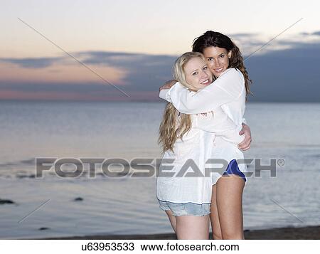 Stock Image - Portrait of two young women friends hugging on beach at dusk, Williamstown, Melbourne, Australia. Fotosearch