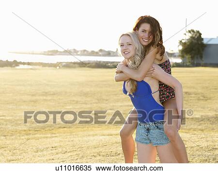 Portrait of two young women friends doing piggyback on beach, Williamstown, Melbourne, Australia View Large Photo Image Stock Photography - Portrait of two young women friends doing piggyback on beach, Williamstown, Melbourne, Australia. Fotosearch