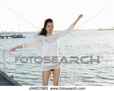Stock Image - Portrait of young woman on beach with arms raised, Port Melbourne, Melbourne, Victoria, Australia. Fotosearch