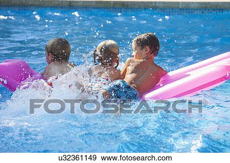 Rear view of three children playing on inflatable mattress in garden swimming pool View Large Photo Image Stock Photo - Rear view of three children playing on inflatable mattress in garden swimming pool. Fotosearch