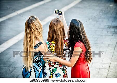 Stock Photo - Rear view of three young women taking selfie with smartphone, Cagliari, Sardinia, Italy. Fotosearch