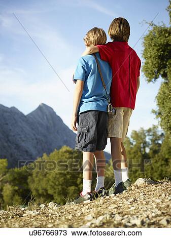 Stock Image - Rear view of two brothers gazing at mountains, Majorca, Spain. Fotosearch