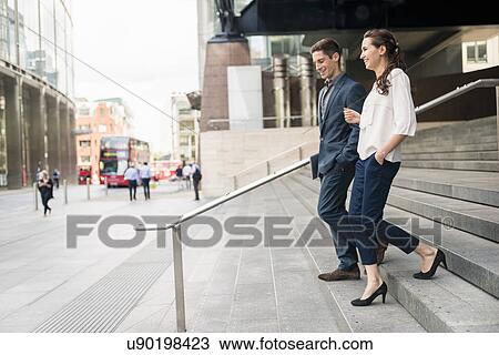 Stock Image - Rear view of young businessman and woman chatting whilst walking down stairway, London, UK. Fotosearch