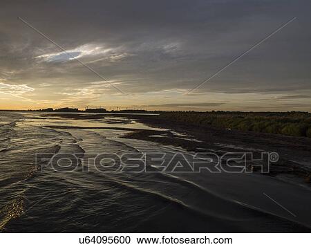 Stock Image - Sea and silhouetted coast at sunrise. Fotosearch
