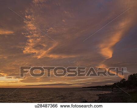 Stock Photograph - Sea and silhouetted coast at sunset. Fotosearch