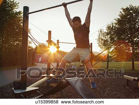 Silhouetted young man swinging on playground climbing frame at sunset View Large Photo Image Stock Photo - Silhouetted young man swinging on playground climbing frame at sunset. Fotosearch