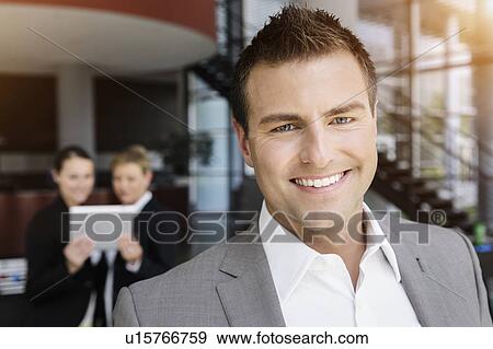 Stock Photo - Smiling businessman, colleagues in background using digital tablet. Fotosearch