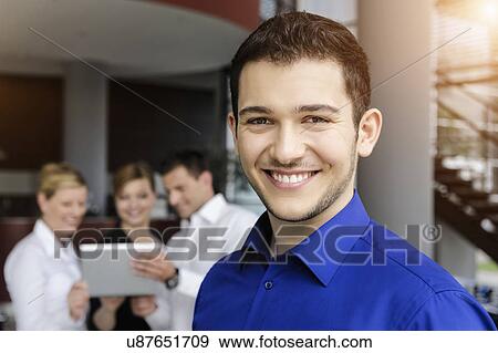 Smiling businessman, colleagues in background using digital tablet View Large Photo Image Stock Photo - Smiling businessman, colleagues in background using digital tablet. Fotosearch