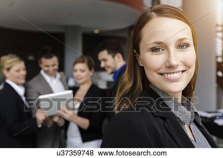 Stock Photo - Smiling businesswoman, colleagues in background using digital tablet. Fotosearch