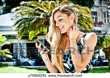 Smiling young woman looking at smartphone in city park View Large Photo Image Stock Photography - Smiling young woman looking at smartphone in city park. Fotosearch