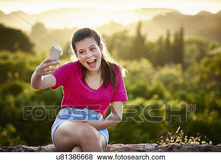 Stock Photo - Teenage girl making face for selfie on smartphone, Majorca, Spain. Fotosearch