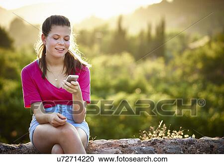 Teenage girl sitting on stone wall looking at smartphone, Majorca, Spain View Large Photo Image Stock Image - Teenage girl sitting on stone wall looking at smartphone, Majorca, Spain. Fotosearch