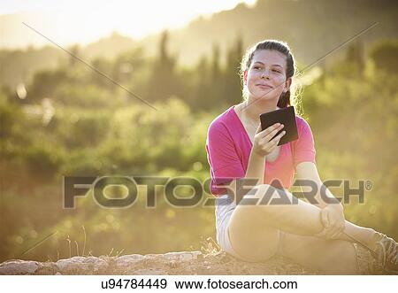 Stock Photo - Teenage girl sitting on stone wall using digital tablet, Majorca, Spain. Fotosearch