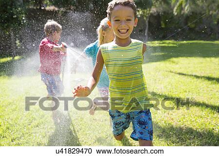 Three children chasing each other in garden with water sprinkler View Large Photo Image Stock Image - Three children chasing each other in garden with water sprinkler. Fotosearch