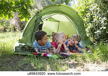 Stock Image - Three children chatting in garden tent. Fotosearch