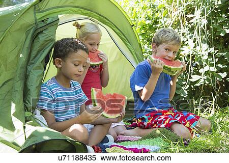 Three children eating watermelon slices in garden tent View Large Photo Image Stock Photography - Three children eating watermelon slices in garden tent. Fotosearch
