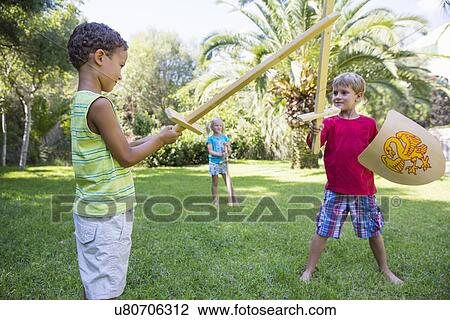Stock Image - Three children in garden playing with toy swords. Fotosearch