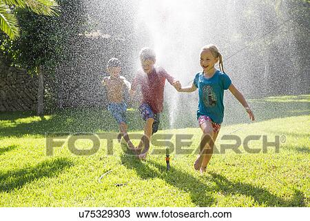 Three children in garden running through water sprinkler View Large Photo Image Stock Image - Three children in garden running through water sprinkler. Fotosearch