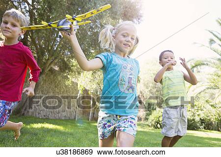 Three children in garden running with toy airplane View Large Photo Image Stock Photo - Three children in garden running with toy airplane. Fotosearch
