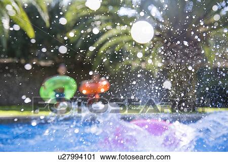 Stock Image - Three children making a splash in garden swimming pool. Fotosearch