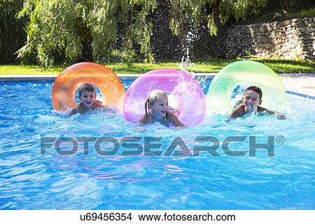 Three children racing on inflatable rings in garden swimming pool View Large Photo Image Picture - Three children racing on inflatable rings in garden swimming pool. Fotosearch