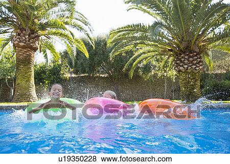 Three children splashing on inflatable rings in garden swimming pool View Large Photo Image Stock Photo - Three children splashing on inflatable rings in garden swimming pool. Fotosearch