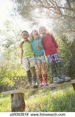 Three children standing on garden seat with arms around each other View Large Photo Image Stock Photo - Three children standing on garden seat with arms around each other. Fotosearch