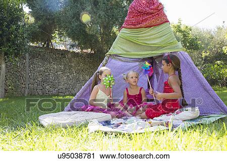 Stock Image - Three girls playing with pin wheels in front of teepee. Fotosearch