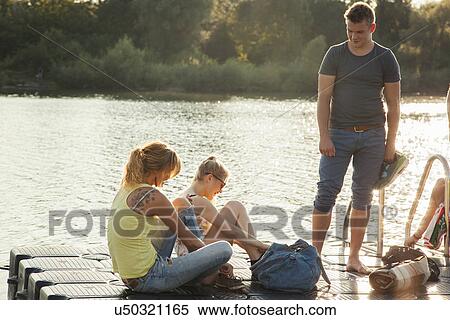 Stock Photography - Three young adult friends tying shoelaces on riverside pier. Fotosearch