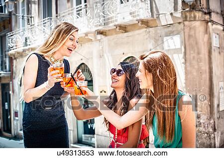 Three young fashionable female friends toasting with cocktails at sidewalk cafe, Cagliari, Sardinia, Italy View Large Photo Image Stock Image - Three young fashionable female friends toasting with cocktails at sidewalk cafe, Cagliari, Sardinia, Italy. Fotosearch