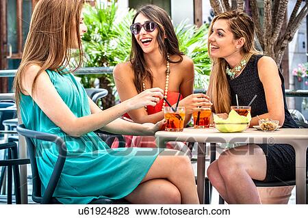 Three young fashionable female friends having cocktails at sidewalk cafe, Cagliari, Sardinia, Italy View Large Photo Image Stock Photo - Three young fashionable female friends having cocktails at sidewalk cafe, Cagliari, Sardinia, Italy. Fotosearch