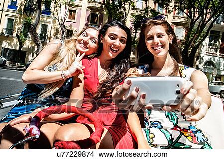 Picture - Three young women taking smartphone selfie on street, Cagliari, Sardinia, Italy. Fotosearch