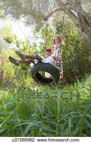 Two girls sitting and standing on tree swing in garden View Large Photo Image Stock Image - Two girls sitting and standing on tree swing in garden. Fotosearch