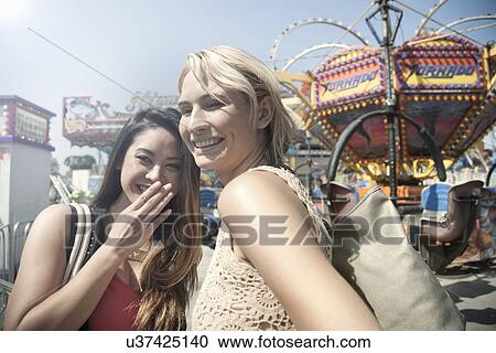 Stock Image - Two women at fairground, laughing and watching surroundings. Fotosearch