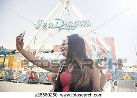 Stock Photo - Two women at fairground, taking self portrait with smart phone. Fotosearch