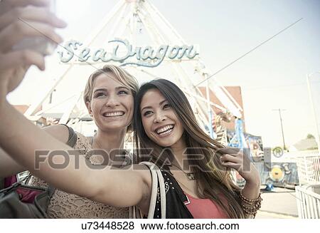 Two women at fairground, taking self portrait with smart phone View Large Photo Image Stock Photo - Two women at fairground, taking self portrait with smart phone. Fotosearch
